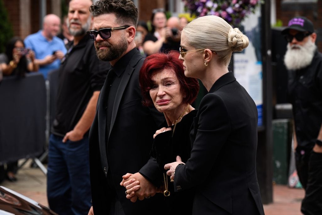 Jack Osbourne, Sharon Osbourne and Kelly Osbourne leave after viewing tributes to the late Ozzy Osbourne from fans as his funeral cortege travels through his home city of Birmingham on July 30, 2025 in Birmingham, England.