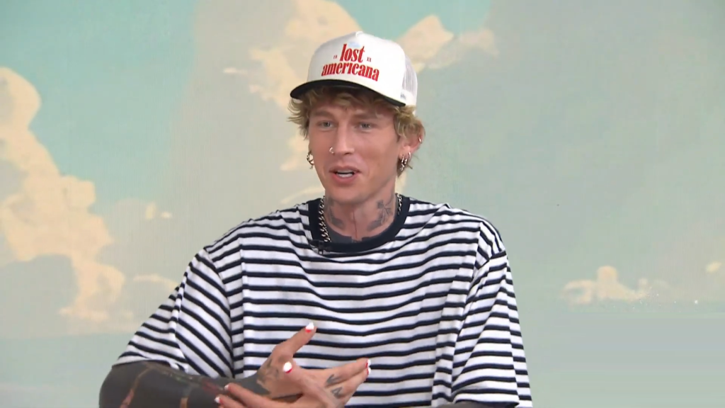 Machine Gun Kelly mimes holding a baby.