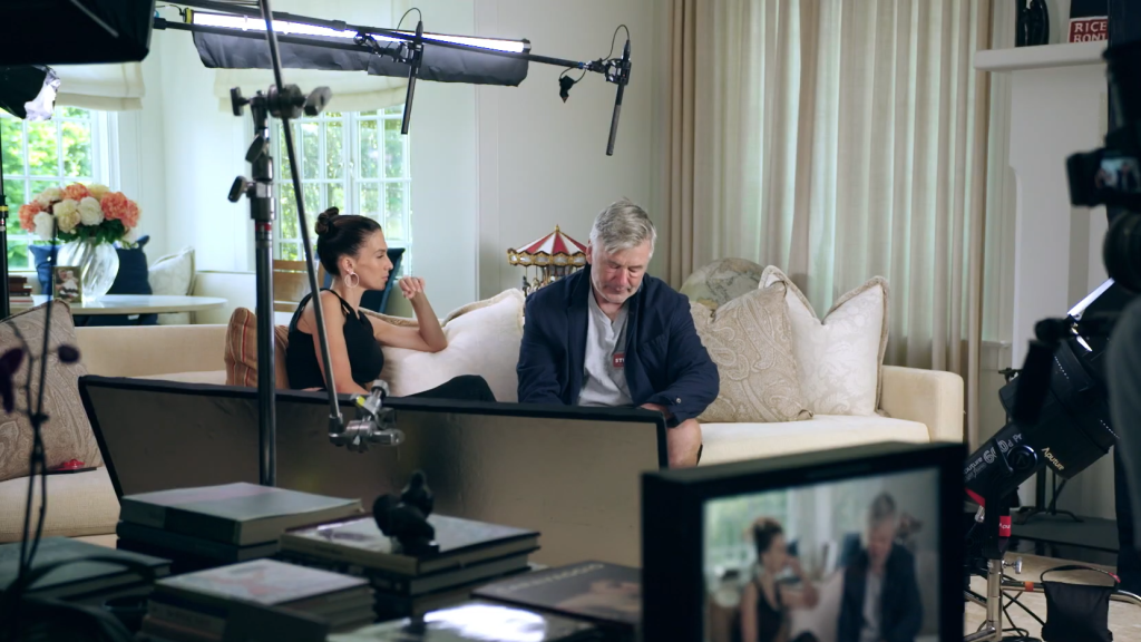 Alec Baldwin and Hilaria Baldwin on The Baldwins, seated on a couch with production equipment visible in the frame.