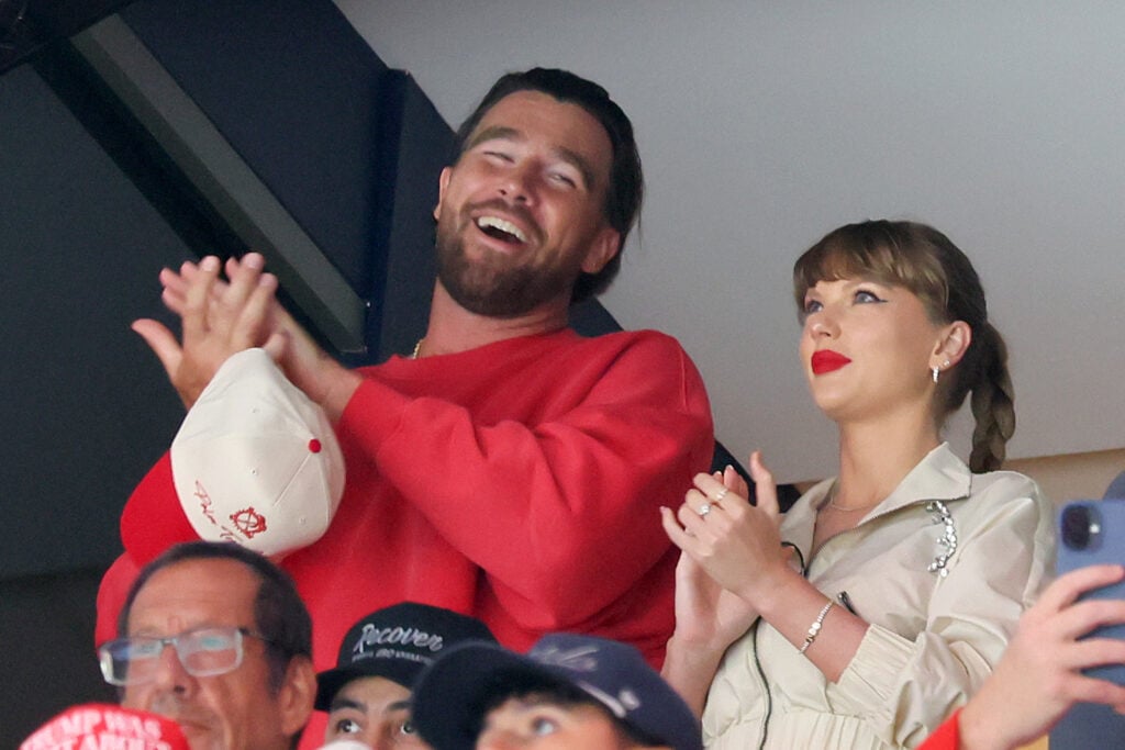 Travis Kelce and Taylor Swift clap watching a game.